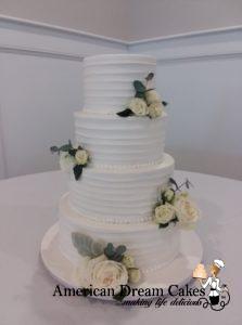 4-tier wedding cake iced in buttercream with horizontal stripes. Decorated with fresh white roses and greenery.